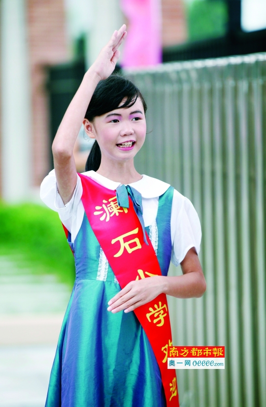 新澜石小学开学第一天,一名女学生站在校门口欢迎同学老师.